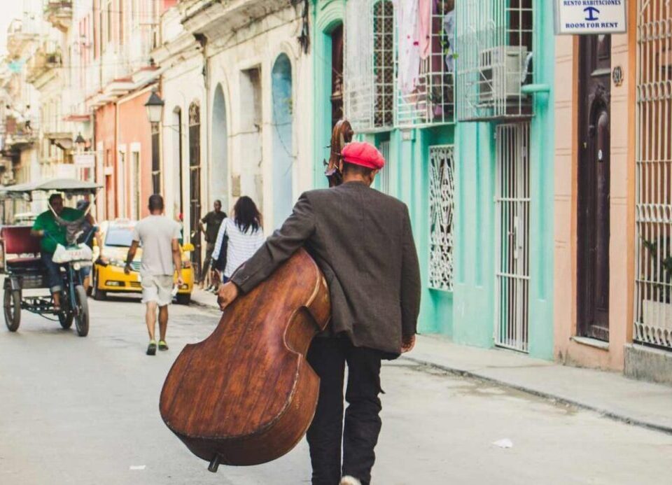 un homme portant une contrebasse se promène dans une ville de Cuba