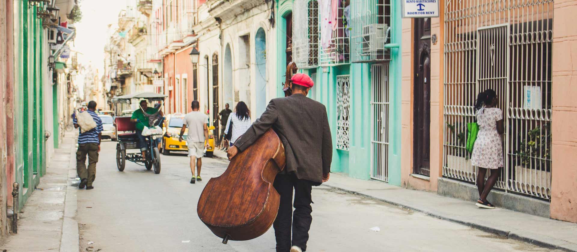 un homme portant une contrebasse se promène dans une ville de Cuba