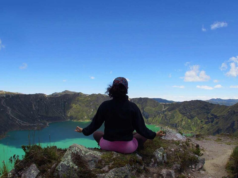 Une femme fait de la méditation au sommet d'une montagne, devant un lac qui est lui aussi au sommet de cette montagne