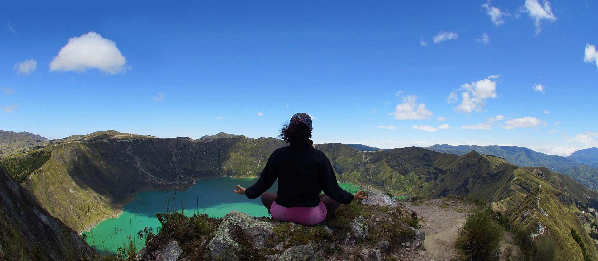 Une femme fait de la méditation au sommet d'une montagne, devant un lac qui est lui aussi au sommet de cette montagne