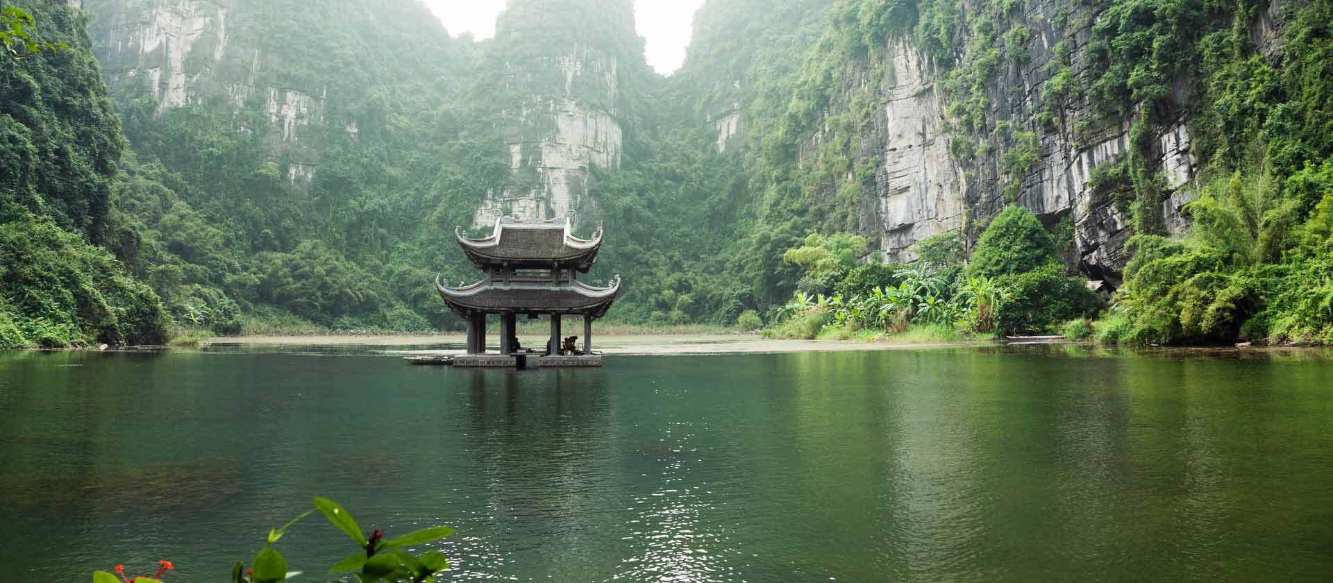 un temple vietnamien au milieu d'un lac entouré de falaises et de nature