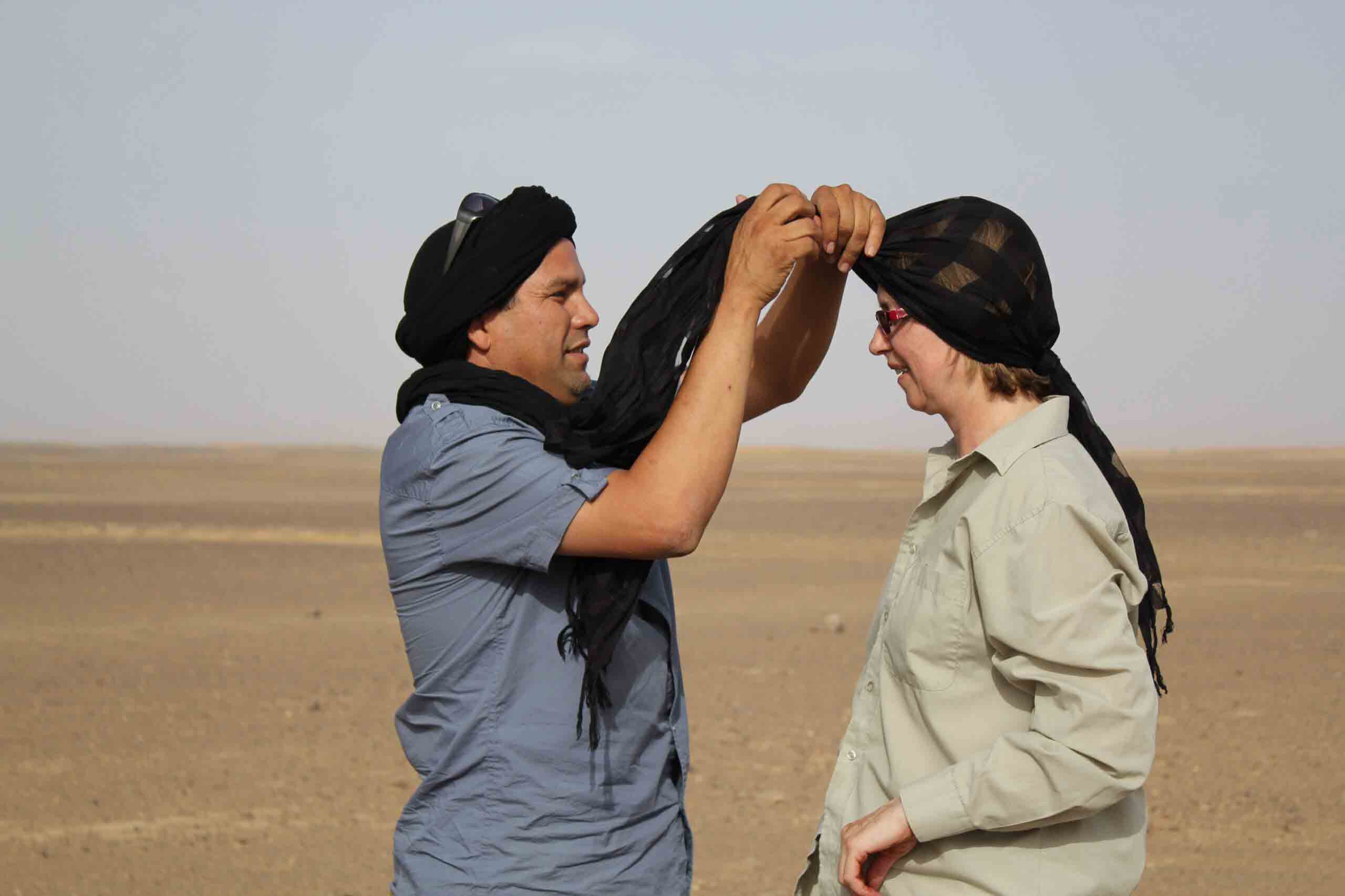 un home marocain couvrant la tête d'une femme blanche avec un foulard noir pour aider avec la chaleur