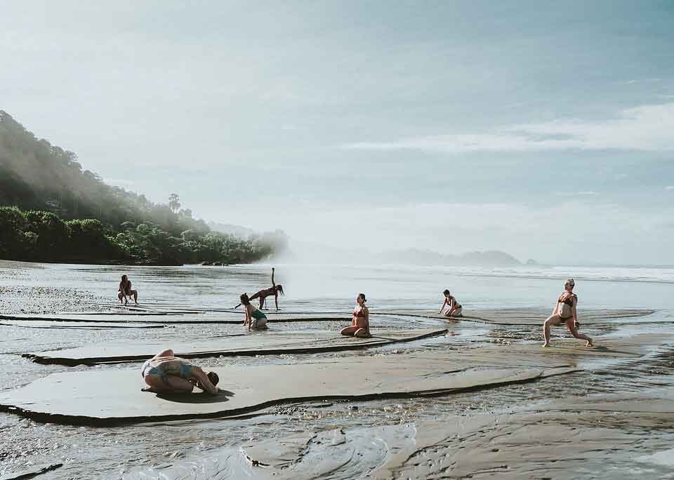 des femmes font du Yoga sur une plage boueuse dans la brume