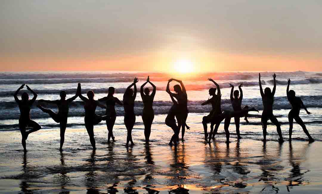 des femmes font du yoga sur la plage face à la lumière du coucher de soleil et aux vagues