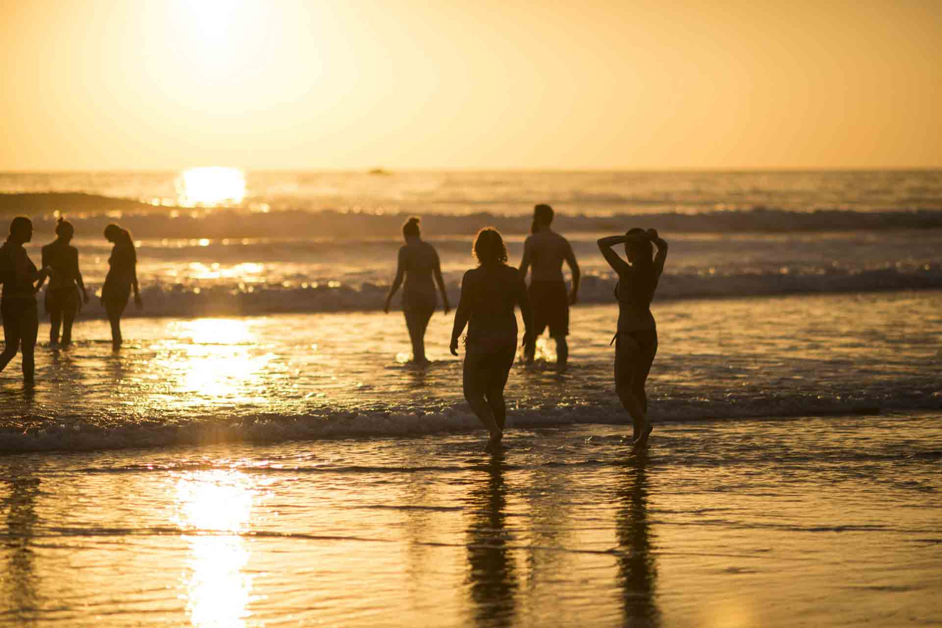 7 personnes sur une plage au coucher de soleil. le soleil est reflété sur l'eau donnant une image à couper le souffle.