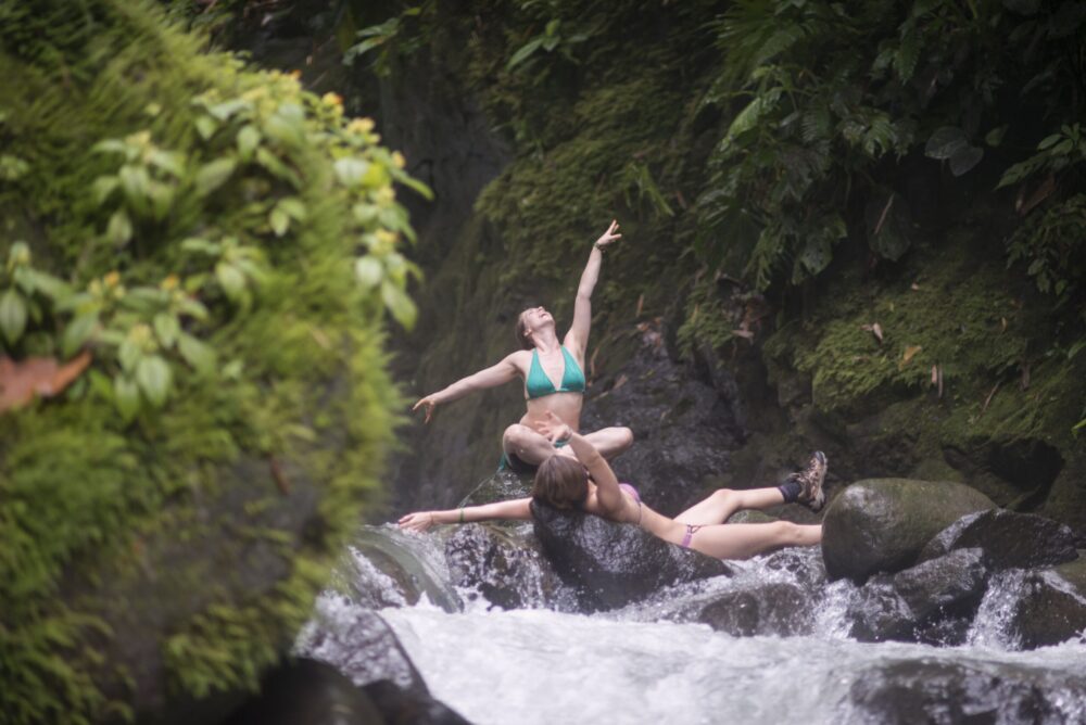 deux femmes en bikini et en soulier font du yoga sur des rochers dans l'eau courante
